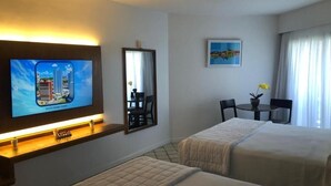 Une chambre d’hôtel avec deux lits, un téléviseur fixé au mur, un bureau avec une chaise, une petite table avec une plante et une fenêtre avec des rideaux.