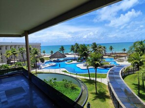 A resort pool area with multiple swimming pools, palm trees, and a view of the ocean. - Hotel Pirâmide Natal (Natal)