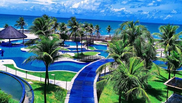 Un complexe hôtelier doté d’une piscine, de palmiers et offrant une vue sur l’océan.