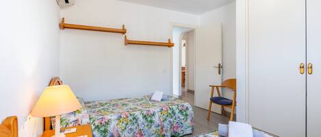 A bedroom with two beds, a chair, a nightstand with a lamp, and a wardrobe.