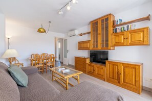 A living room with a sofa, coffee table, wooden cabinets, a TV, and a dining area with chairs and a table.
