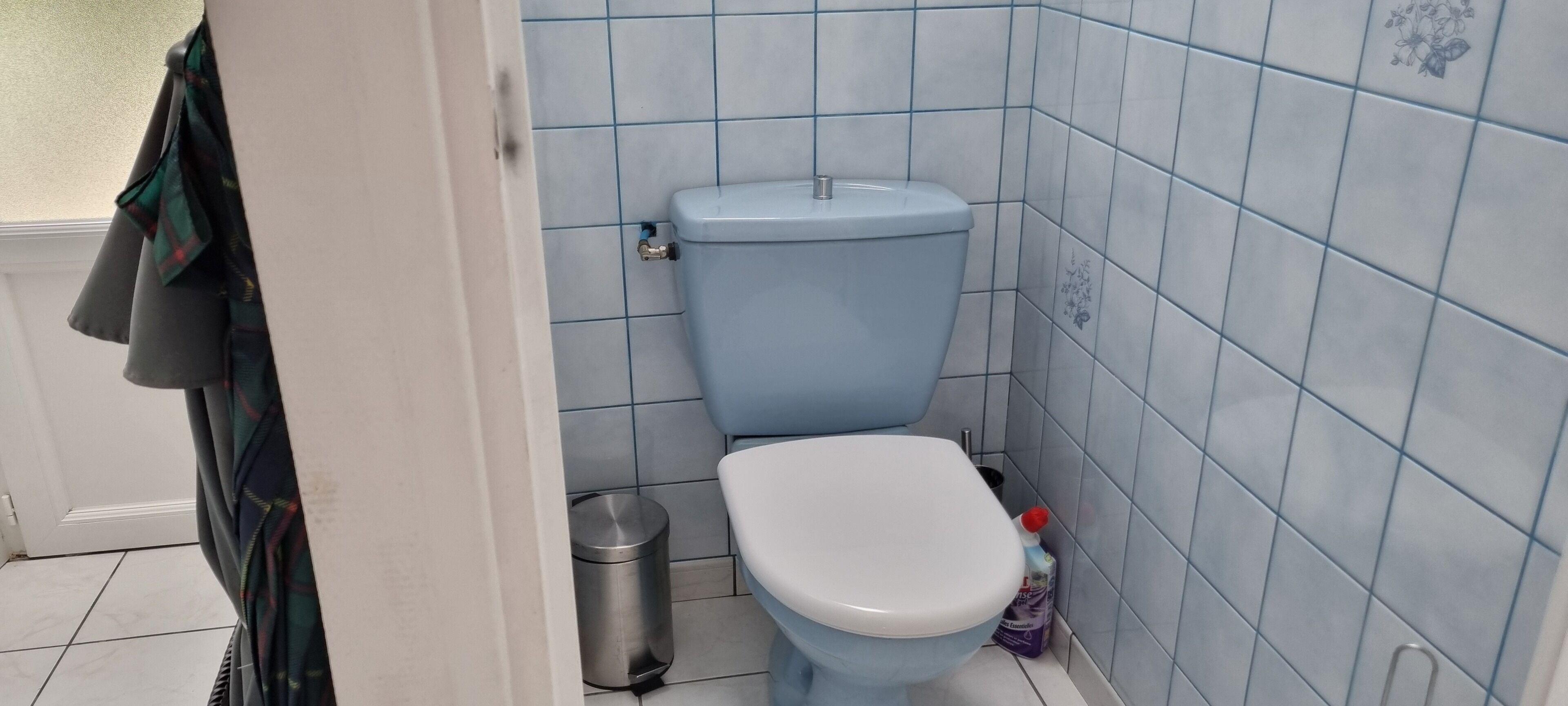 A bathroom with a toilet, a trash bin, and a bottle of cleaning product.