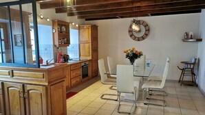A modern kitchen with wooden cabinets, a dining table with white chairs, and a large wall clock.