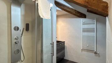 Un baño moderno con cabina de ducha de vidrio, toallero empotrado y techo con vigas de madera.