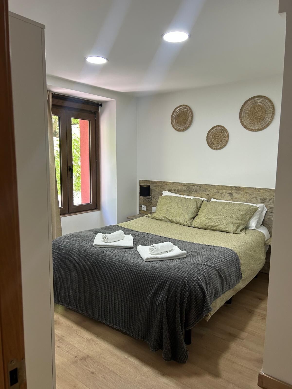 Un dormitori amb un llit, dues decoracions circulars penjades a la paret, una finestra amb cortines i una porta.