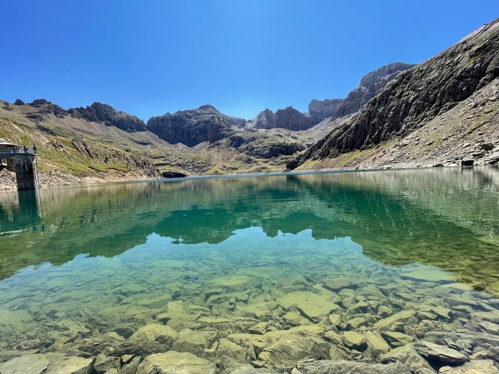 Ein klarer Bergsee mit steinigen Ufern und einer Brücke.