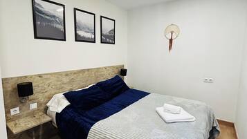 A neatly arranged bedroom with a bed, a nightstand, a wall-mounted lamp, and framed pictures on the wall.