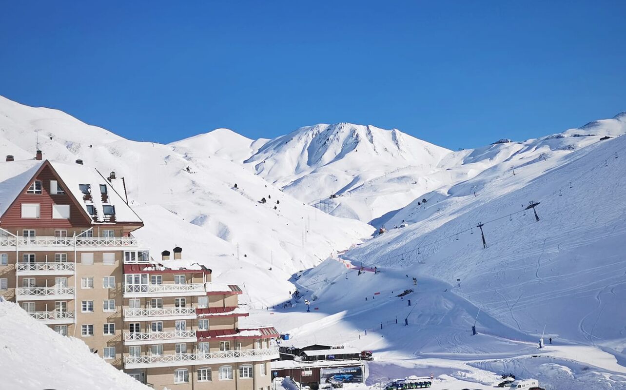 Une montagne enneigée, avec un télésiège et un bâtiment doté de balcons.