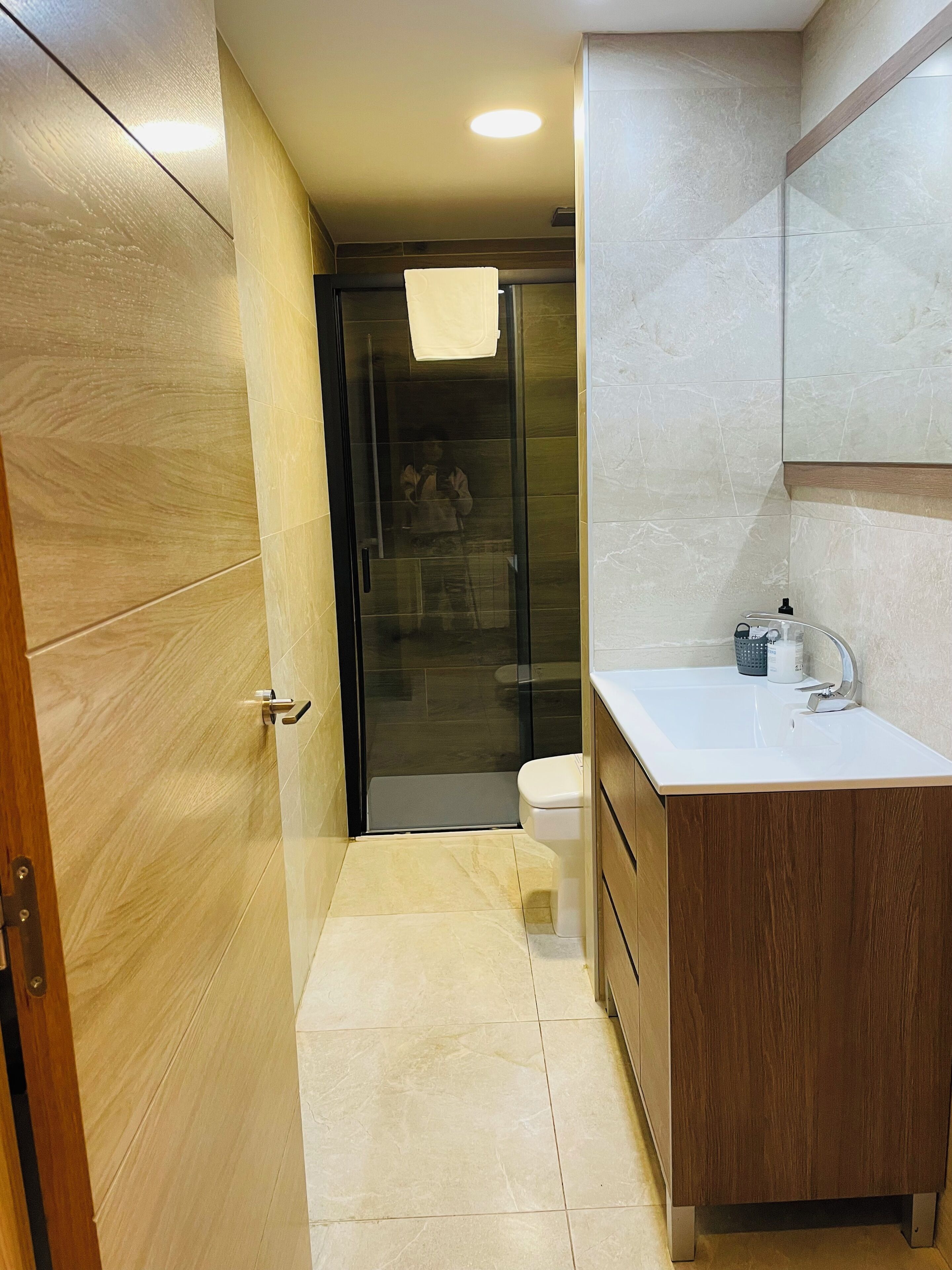 A modern bathroom with a glass shower enclosure, a white sink, and wooden cabinetry.