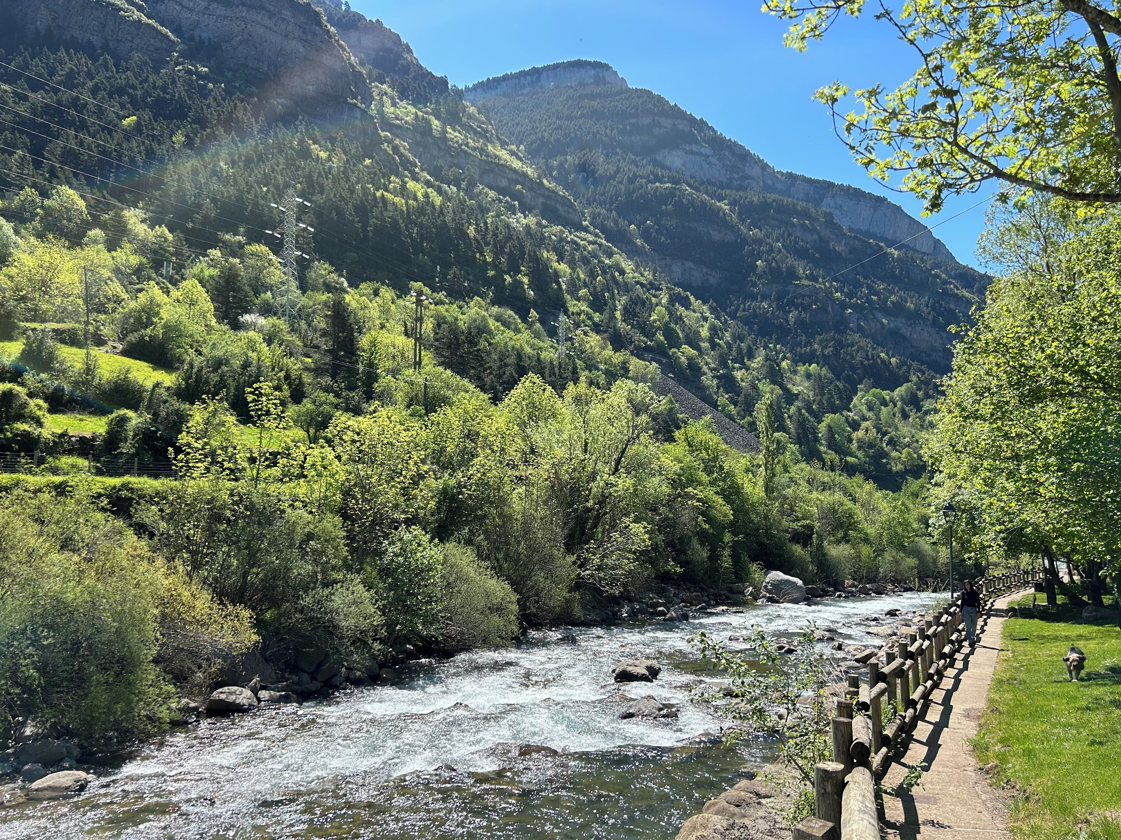 A river flowing through a mountainous area with a wooden walkway along the riverbank.