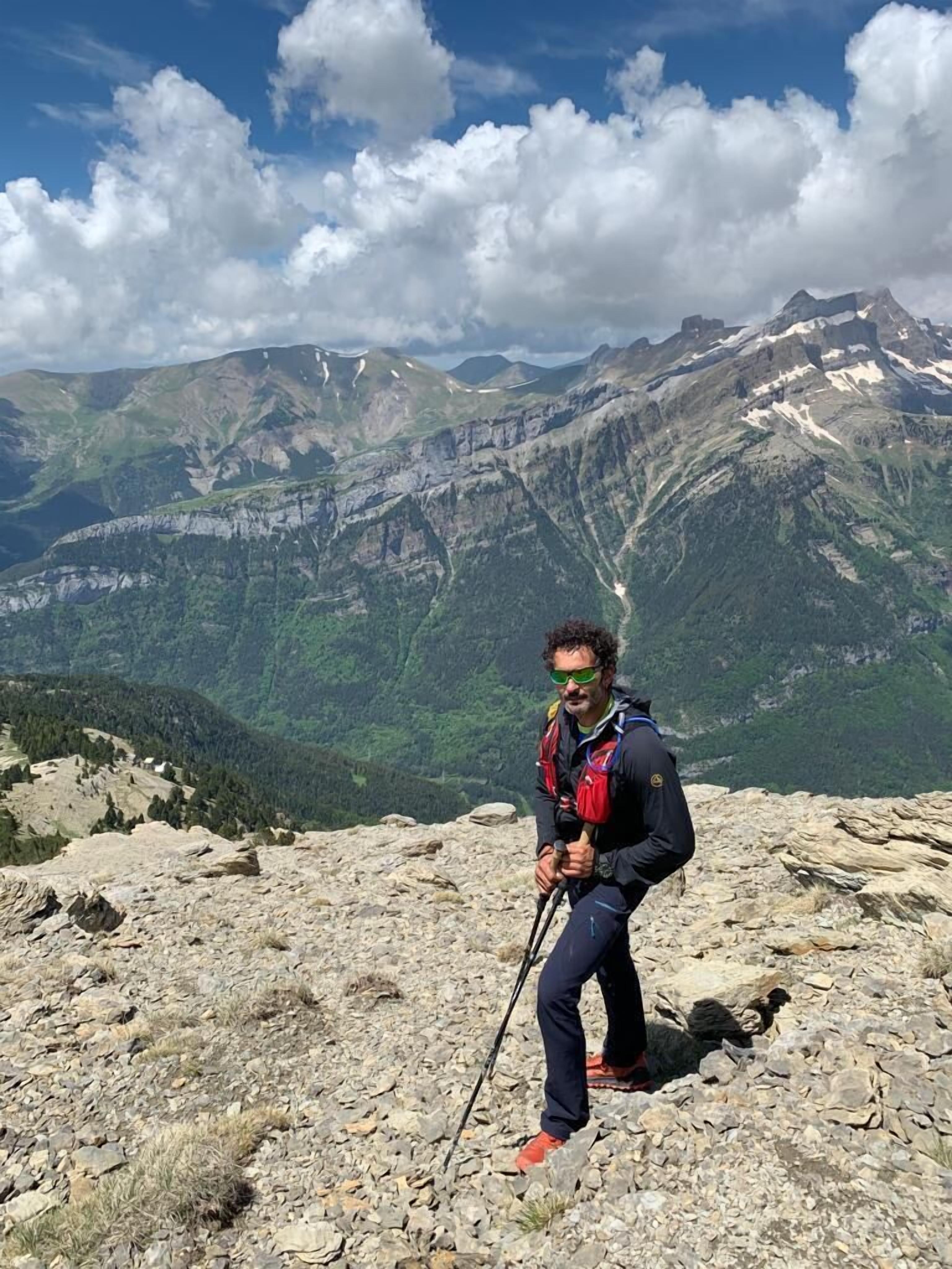 A hiker on a rocky mountain peak with a view of a valley and distant mountains.