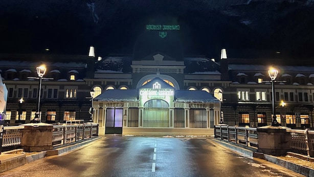 A hotel entrance with a snow-covered mountain backdrop, illuminated by street lamps. - Apartahotel Canfranc (Canfranc)