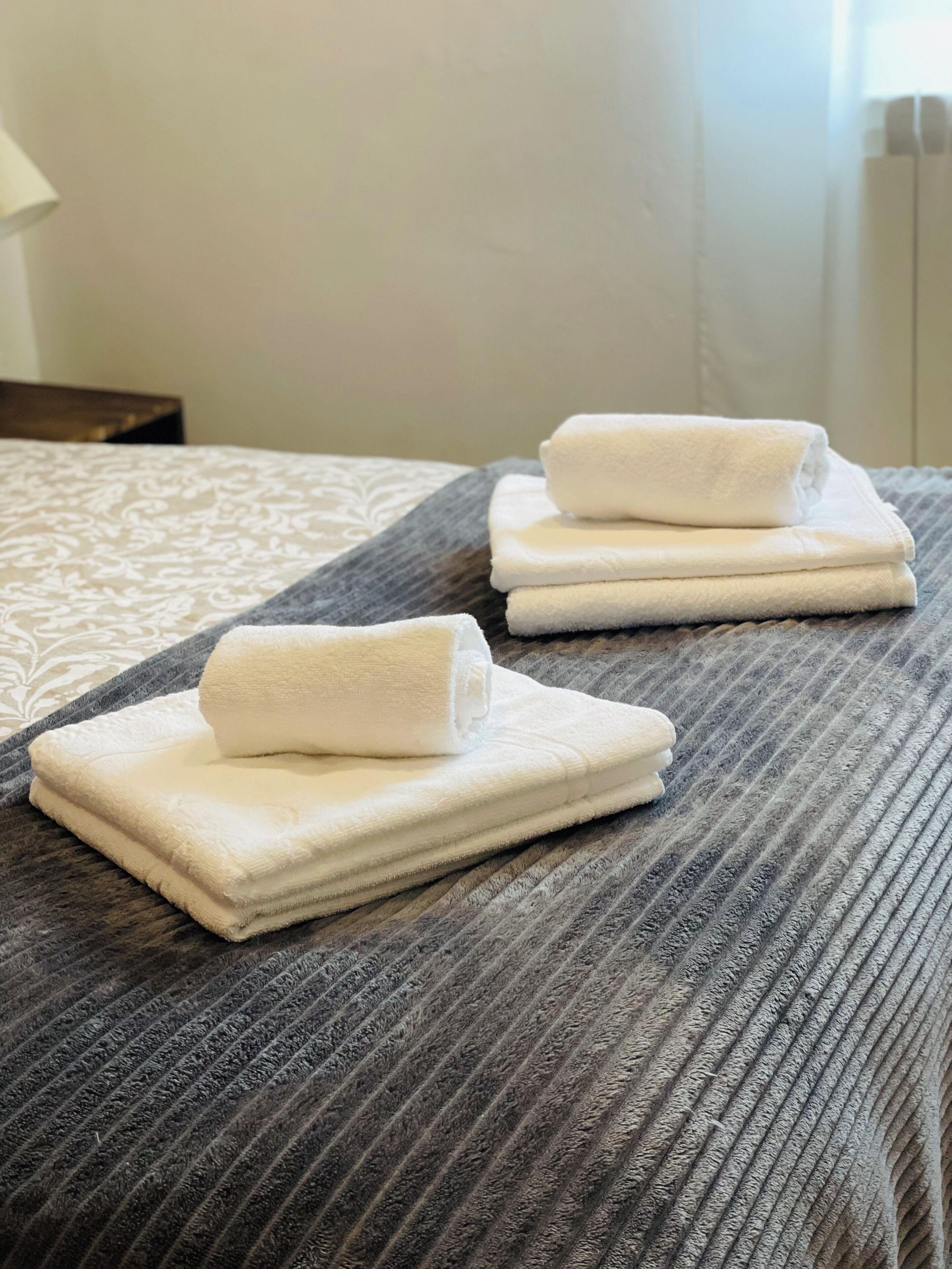 Ein ordentlich bezogenes Bett mit einer grauen, strukturierten Bettdecke und einem weißen Kissen mit Muster.