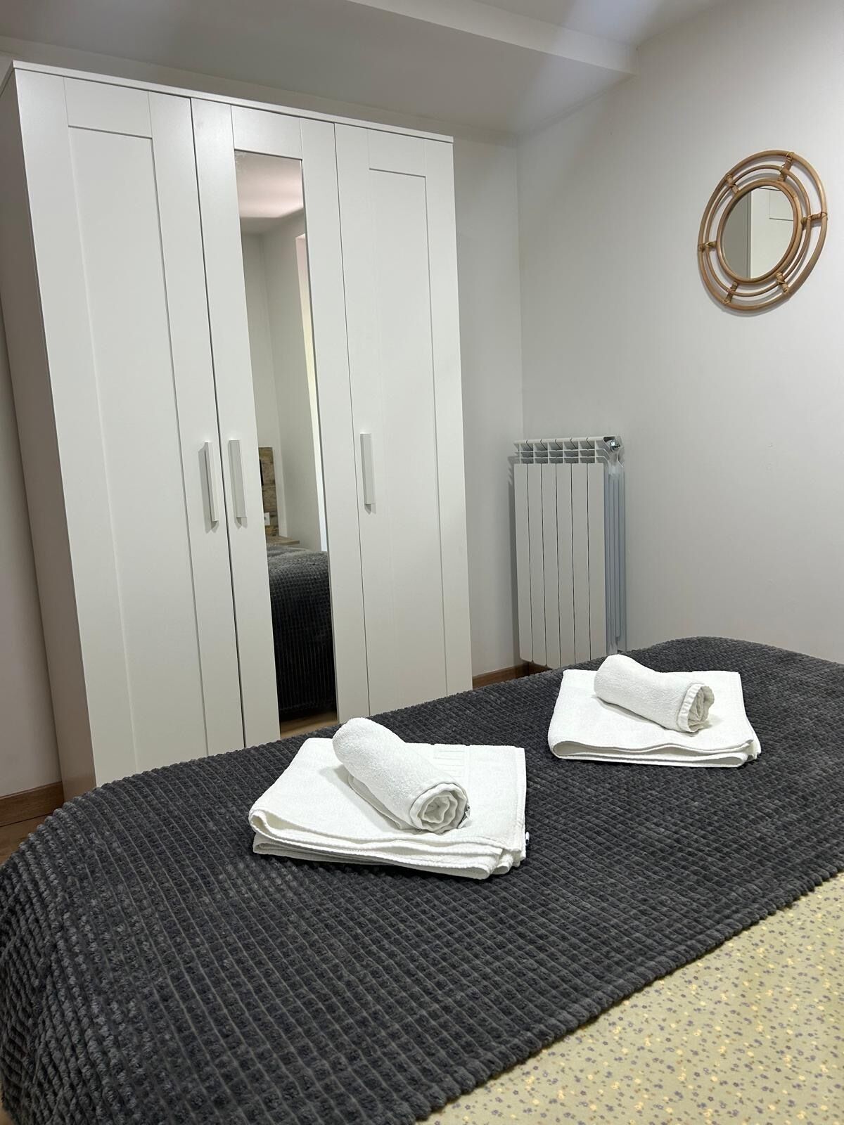 Een slaapkamer met een bed, een kledingkast, een radiator en een spiegel aan de muur.