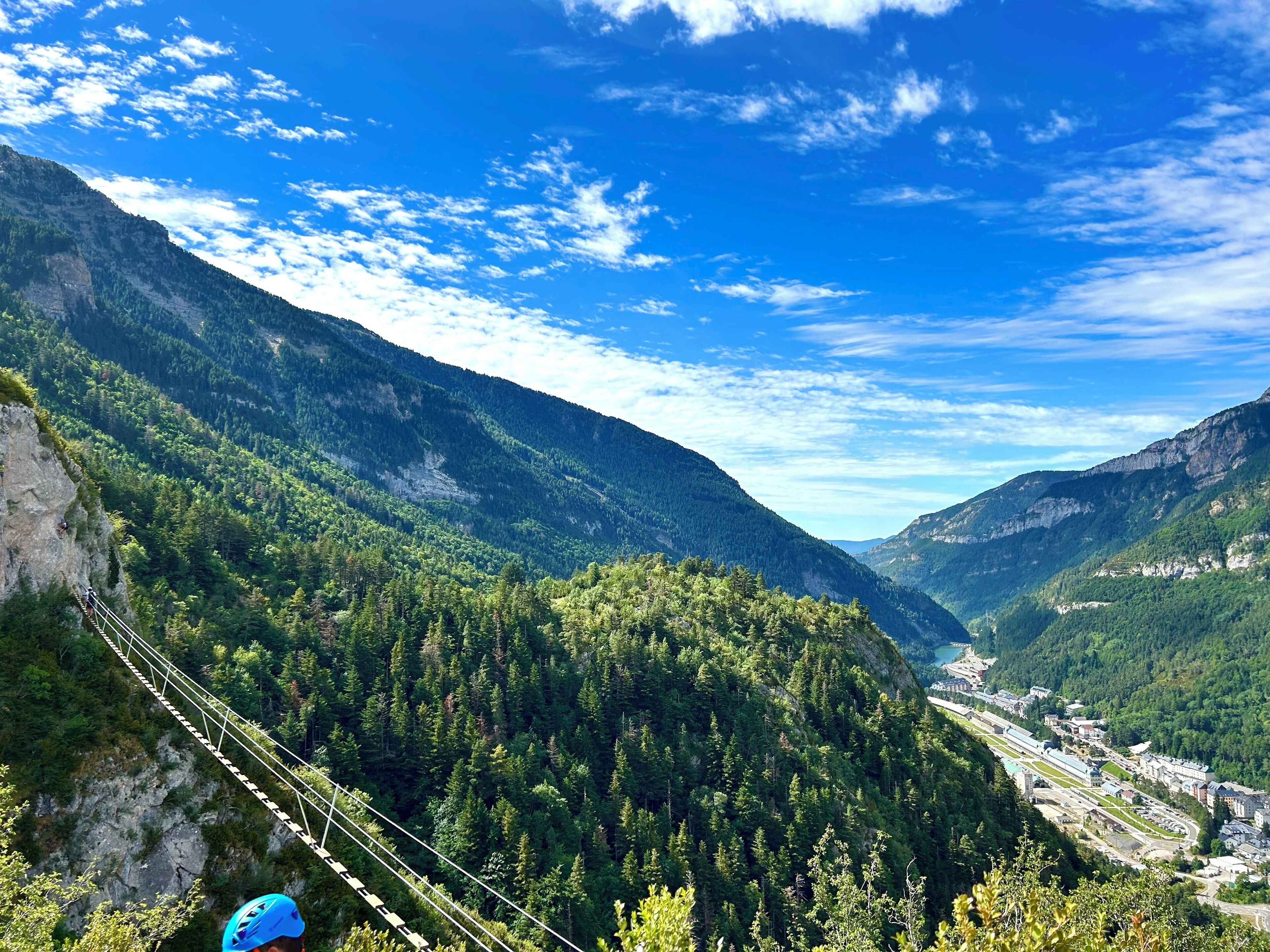 A mountainous landscape with a suspension bridge, dense forest, and a valley with buildings.