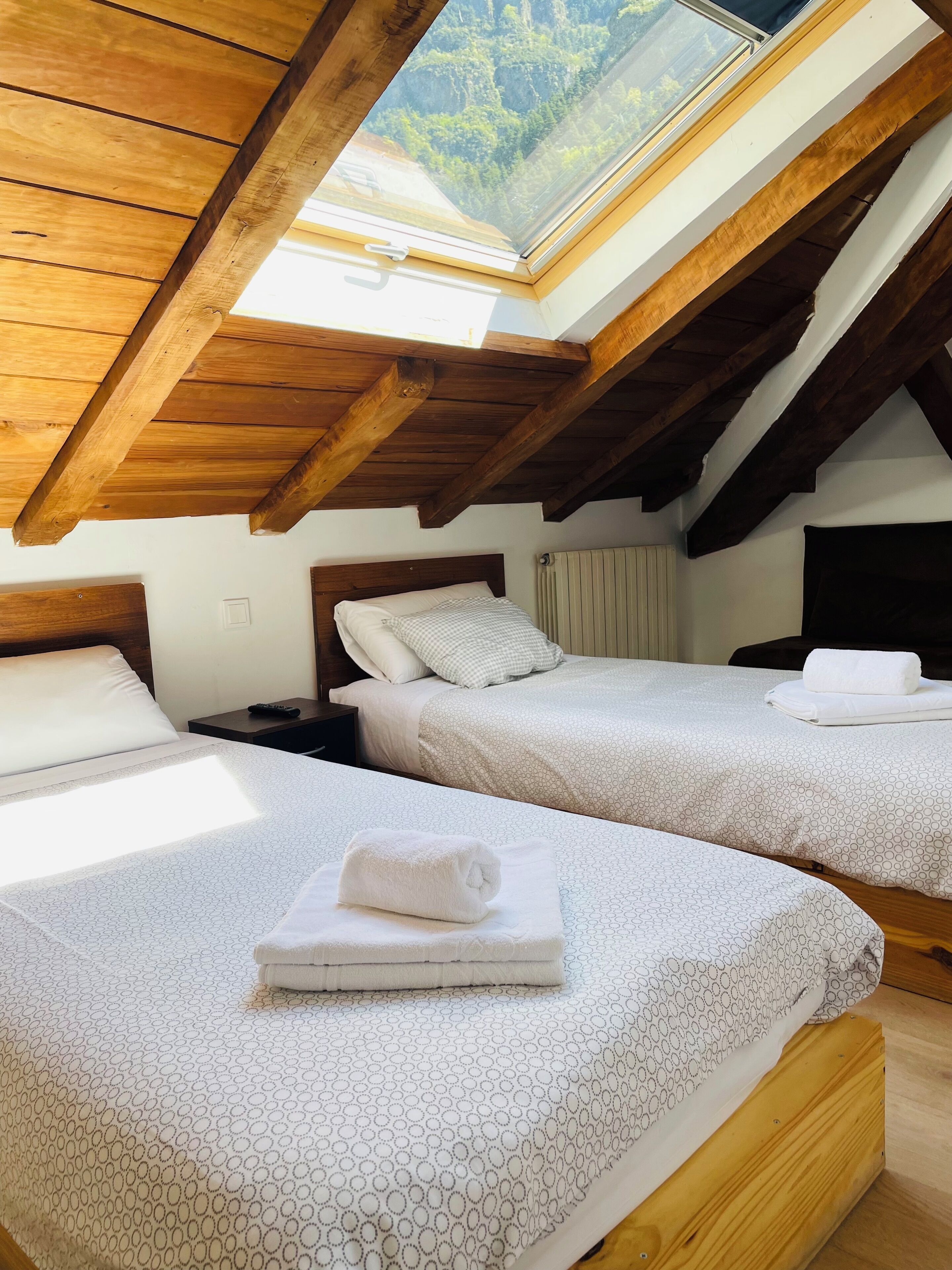 Ein Schlafzimmer mit zwei Betten, einem Oberlicht, Holzbalken und Blick ins Freie.