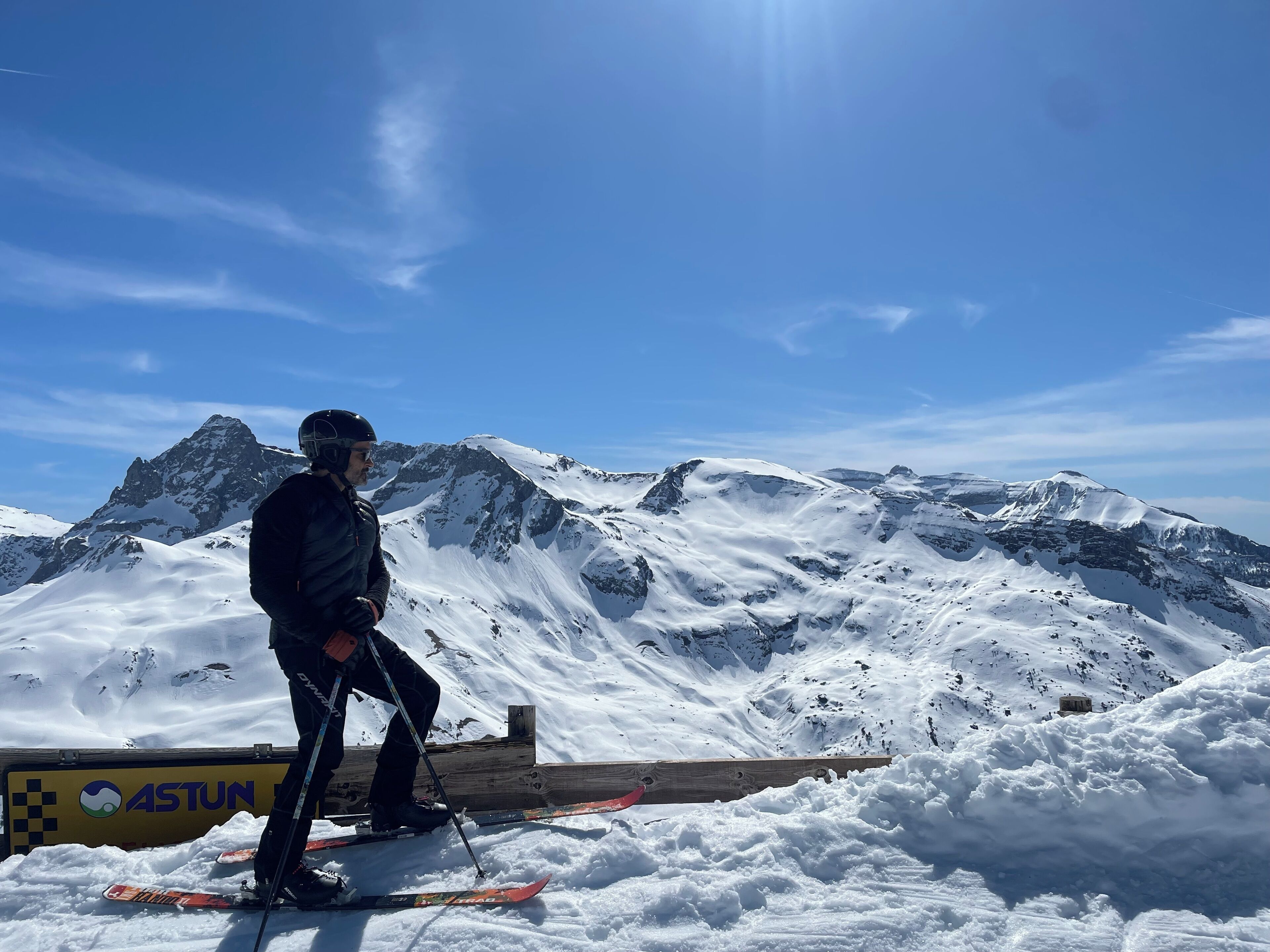 Une personne faisant du ski sur une montagne enneigée, avec une rampe en bois et un panneau portant le logo « ASTUN ».