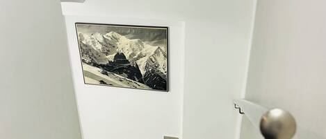 A staircase with a black and white striped floor, a framed picture of a mountain landscape on the wall, and a door with a round handle.
