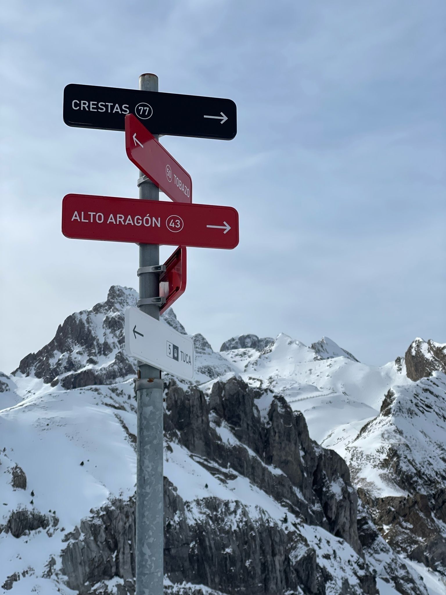 A directional signpost with multiple route indicators for Crestas 77, Alto Aragon 43, and Tuca 5.