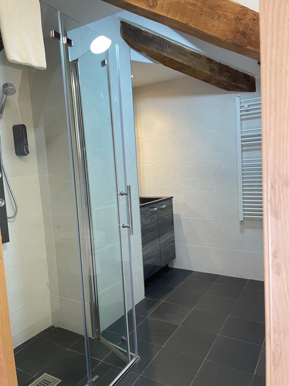 A modern bathroom with a glass shower enclosure, a vanity with a mirror, and a towel hanging on the wall.