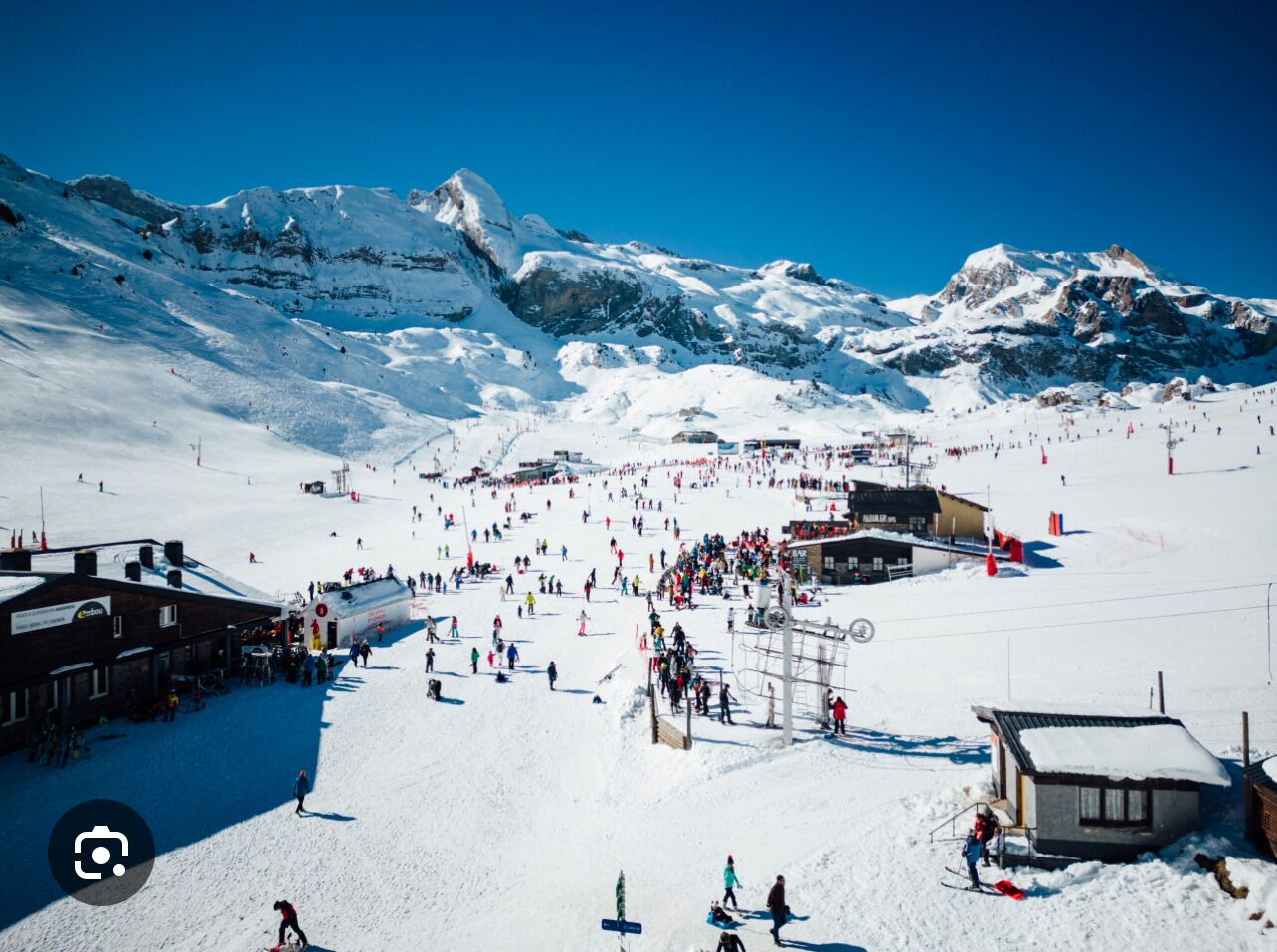 Une station de ski enneigée, avec un télésiège, des bâtiments et un paysage montagneux en arrière-plan.