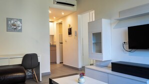 A modern living room with a sofa, a coffee table with a vase, a flat-screen TV mounted on the wall, and a kitchen area in the background. - Makhoul 310 (Beirut)