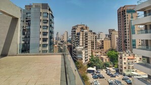 A high-rise building with multiple floors, large windows, and a parking area with several cars. - Makhoul 310 (Beirut)