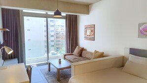 A modern hotel room with a sofa, a bed, a desk, and a large window offering a view of the cityscape. - Makhoul 310 (Beirut)