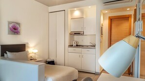 A hotel room with a bed, bedside table, lamp, and a kitchenette area with cabinets and a stove. - Makhoul 310 (Beirut)
