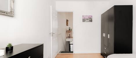 A bedroom with a black wardrobe, a bed with white bedding, a black dresser, and a small potted plant.