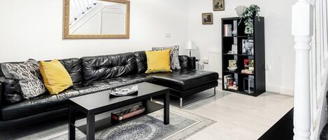 A modern living room with a black leather sofa, a coffee table, and a black bookshelf.