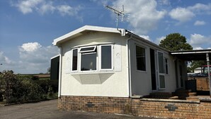 A small, single-story house with a sloped roof, a satellite dish on the roof, and a brick foundation. - 2 Bed Chalet on Working Farm (Cullompton)