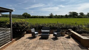 A patio with wicker furniture overlooking a green field with sheep. - 2 Bed Chalet on Working Farm (Cullompton)