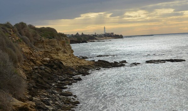 Un paisaje costero con acantilados rocosos, un faro y un mar tranquilo bajo un cielo nublado.