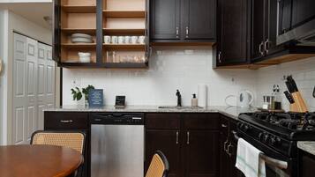 Una cocina con armarios oscuros, un lavavajillas de acero inoxidable, una estufa a gas y un comedor con mesa y sillas de madera.