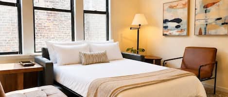 Habitación de hotel con una cama grande, un escritorio, una silla, una lámpara y obras de arte en la pared.