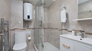 Un baño moderno con inodoro, ducha con mampara de vidrio, lavamanos y perchero para toallas.