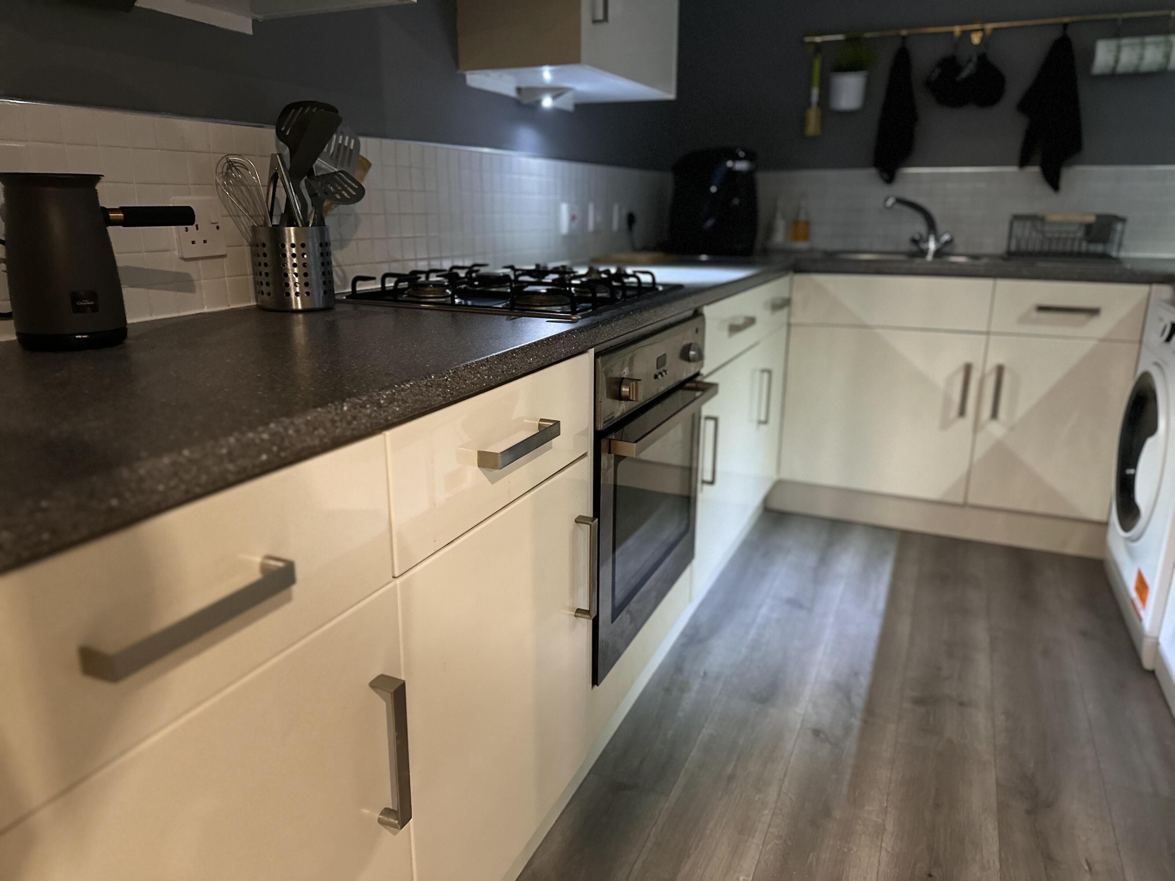 Une cuisine moderne avec des meubles blancs, une cuisinière à gaz, un four et un lave-linge encastré.