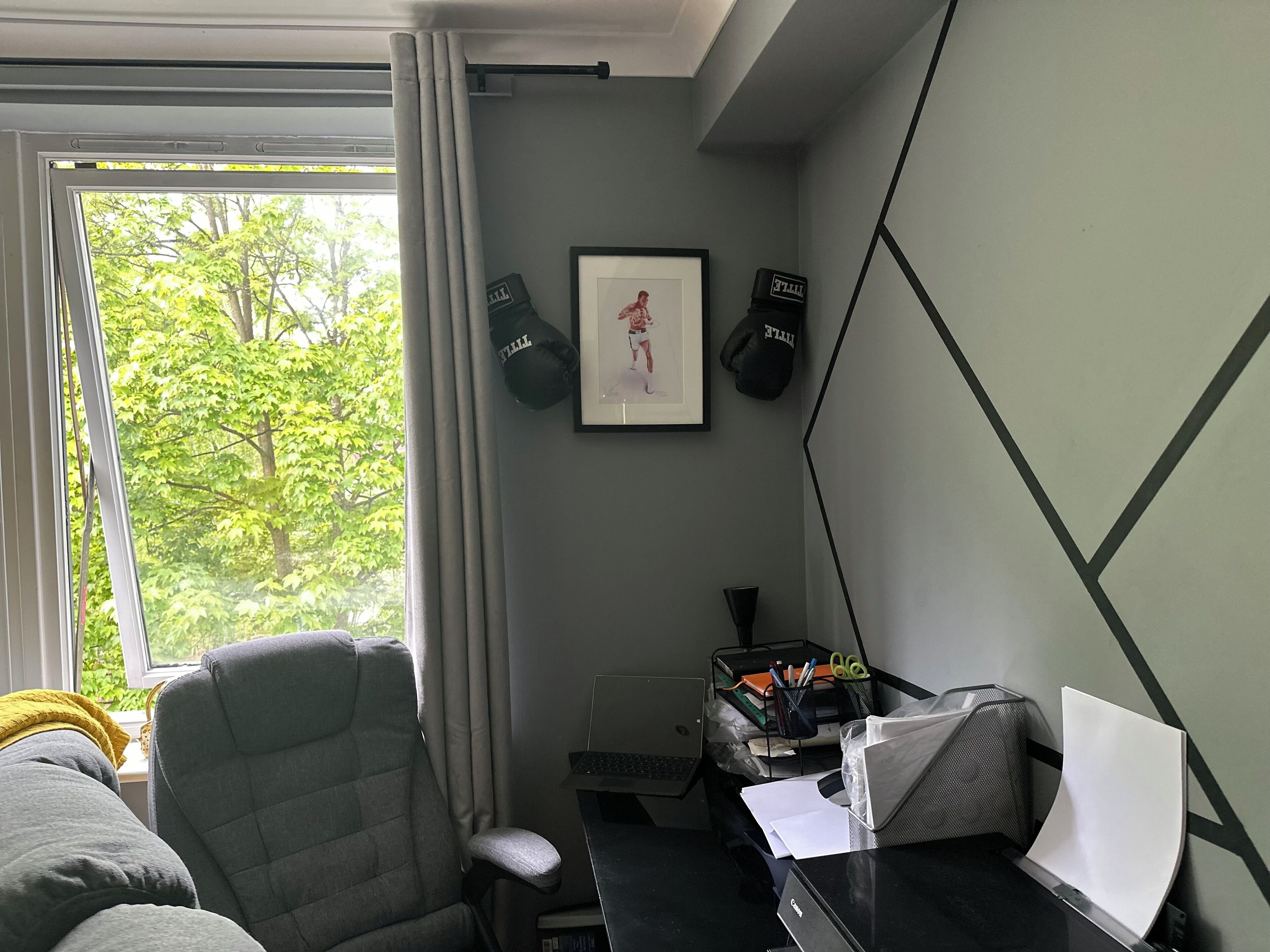 Une chambre d’hôtel avec un bureau, une chaise et une fenêtre donnant sur des arbres. Deux sacs noirs sont accrochés au mur, ainsi qu’un tableau encadré.
