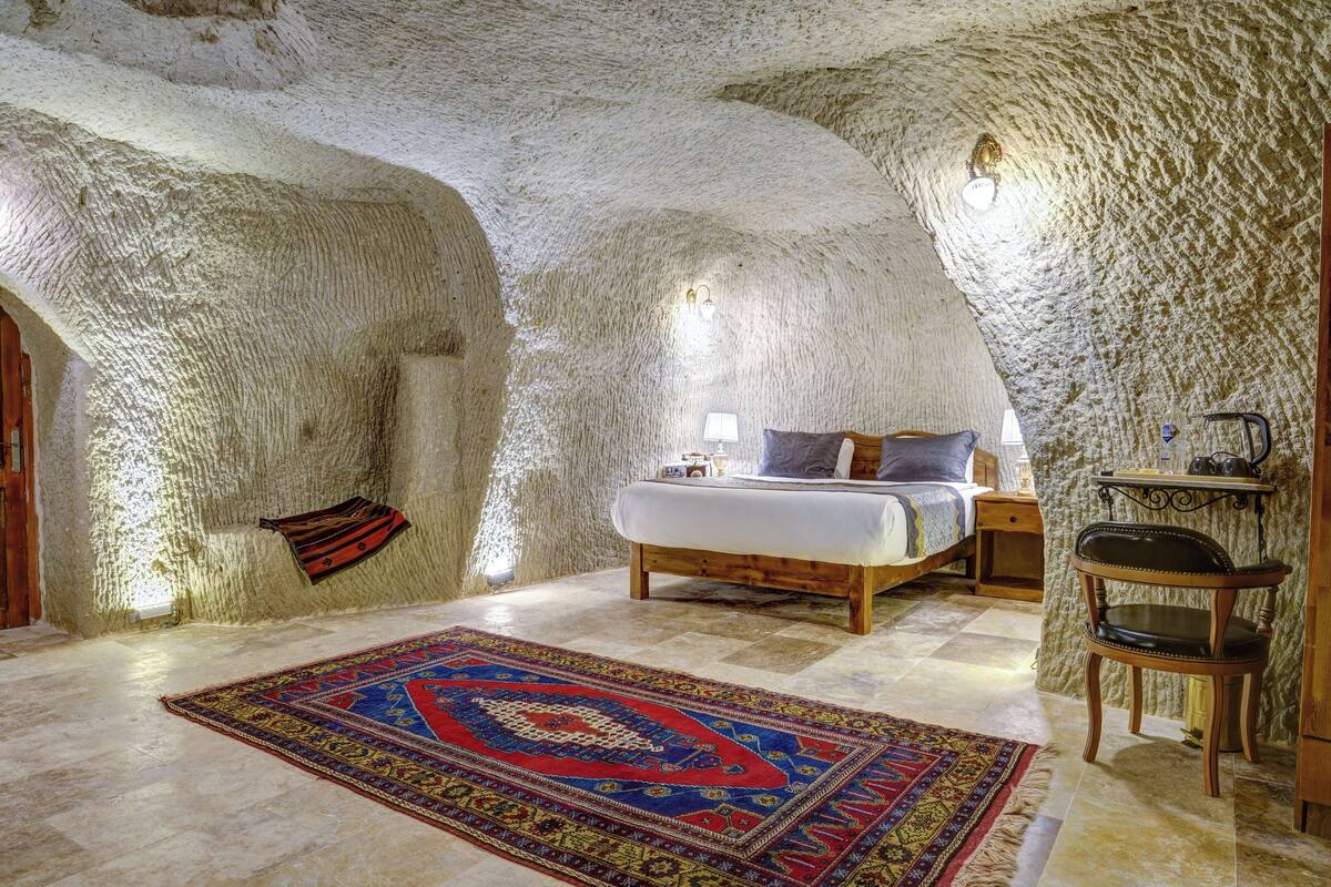 Ein Schlafzimmer mit Bett, Nachttisch, Lampe, Stuhl und Teppich in einer höhlenartigen Einrichtung.