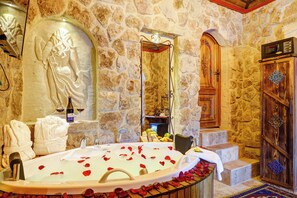 Ein Badezimmer mit Steinwänden, einer Badewanne, Handtüchern und einem Holzschrank.