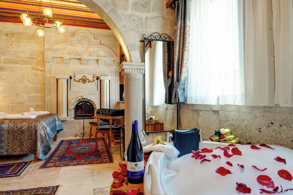 Ein luxuriöses Zimmer mit Bett, Kamin, Essbereich und großem Fenster mit Vorhängen.