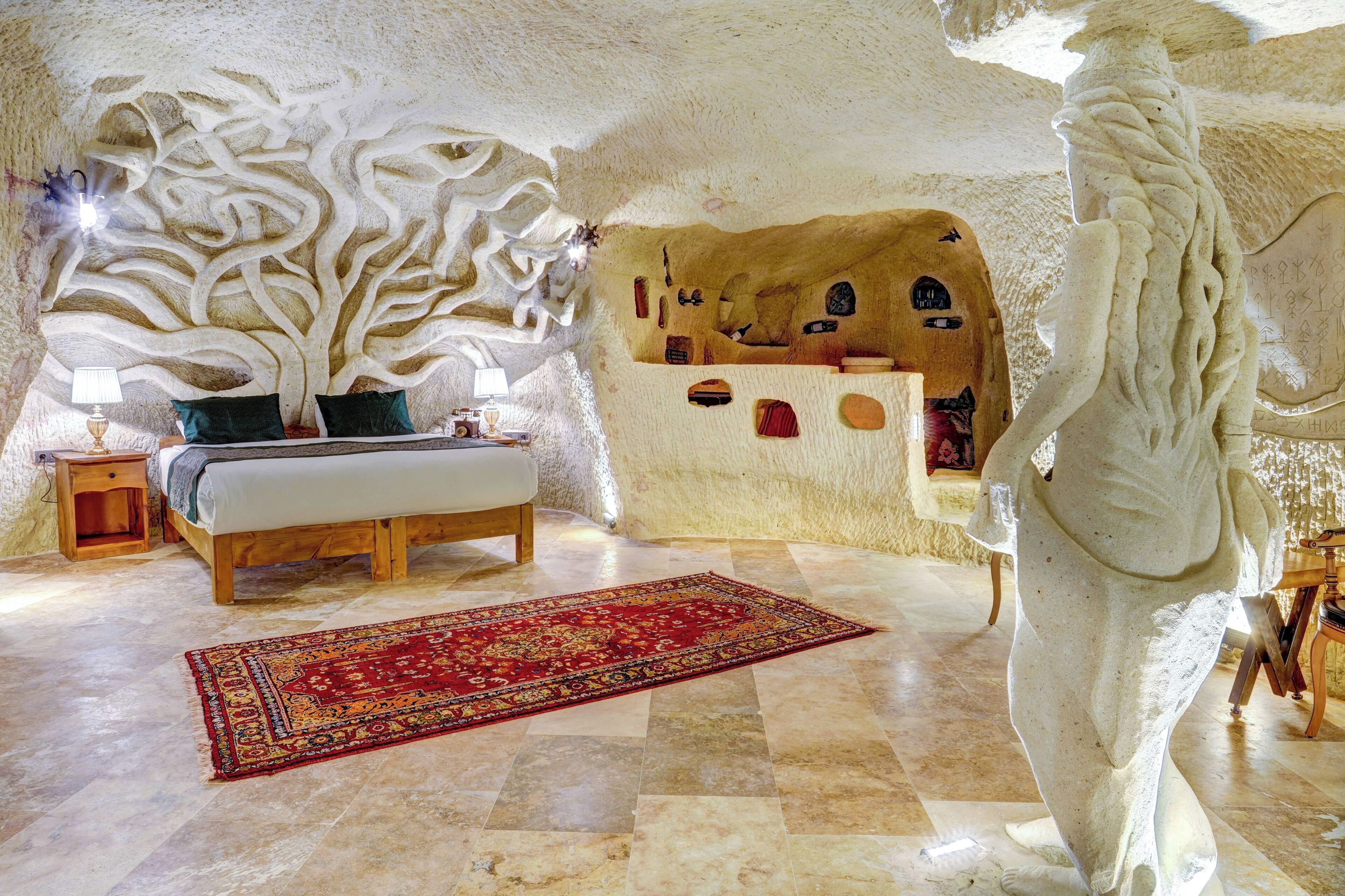 Una habitació amb un mural gran de paisatge arboreu, un llit, una catifa vermella i una estàtua de pedra.