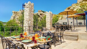 An outdoor dining area with stone pillars, metal chairs, and umbrellas. Tables are set with plates, cutlery, and drinks. - Marbay Cave Cappadocia (Nevsehir)