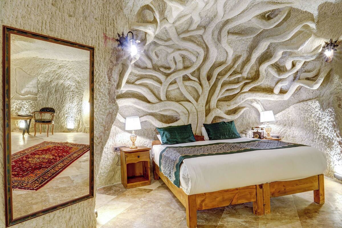 Ein Schlafzimmer mit einem großen Spiegel, einem Bett mit Holzrahmen, einem Nachttisch und einer Wand mit einem baumartigen Design.