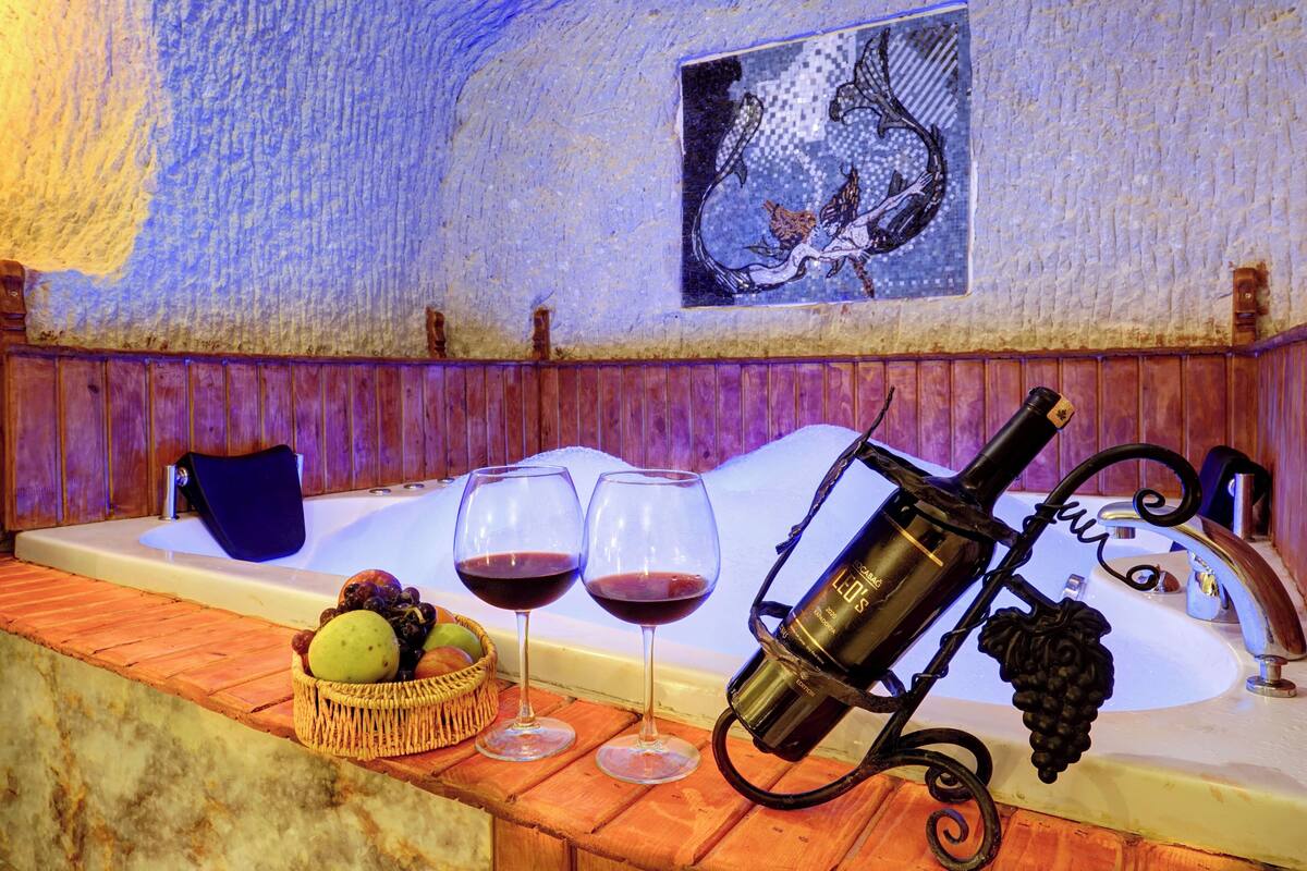 Ein Zimmer mit einer Badewanne, zwei Weingläsern, einer Weinflasche und einem Obstkorb.