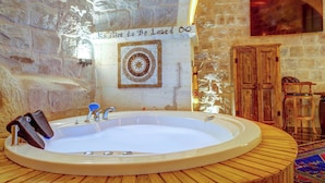 A stone-walled bathroom with a large bathtub, wooden furniture, and a decorative wall piece. - Marbay Cave Cappadocia (Nevsehir)