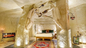 A room with a bed, a fireplace, a rug, and a small refrigerator. - Marbay Cave Cappadocia (Nevsehir)