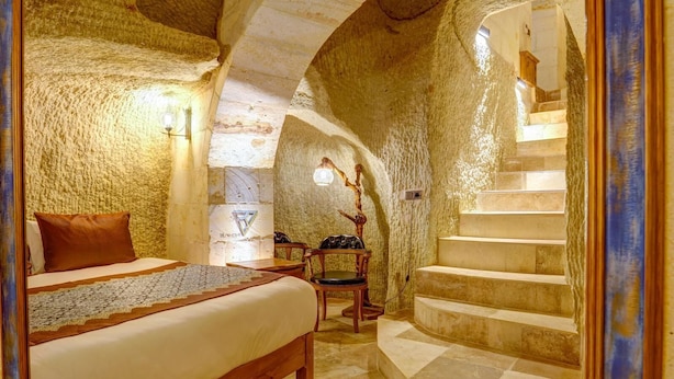 A rustic stone room with a bed, a chair, and a staircase. - Marbay Cave Cappadocia (Nevsehir)