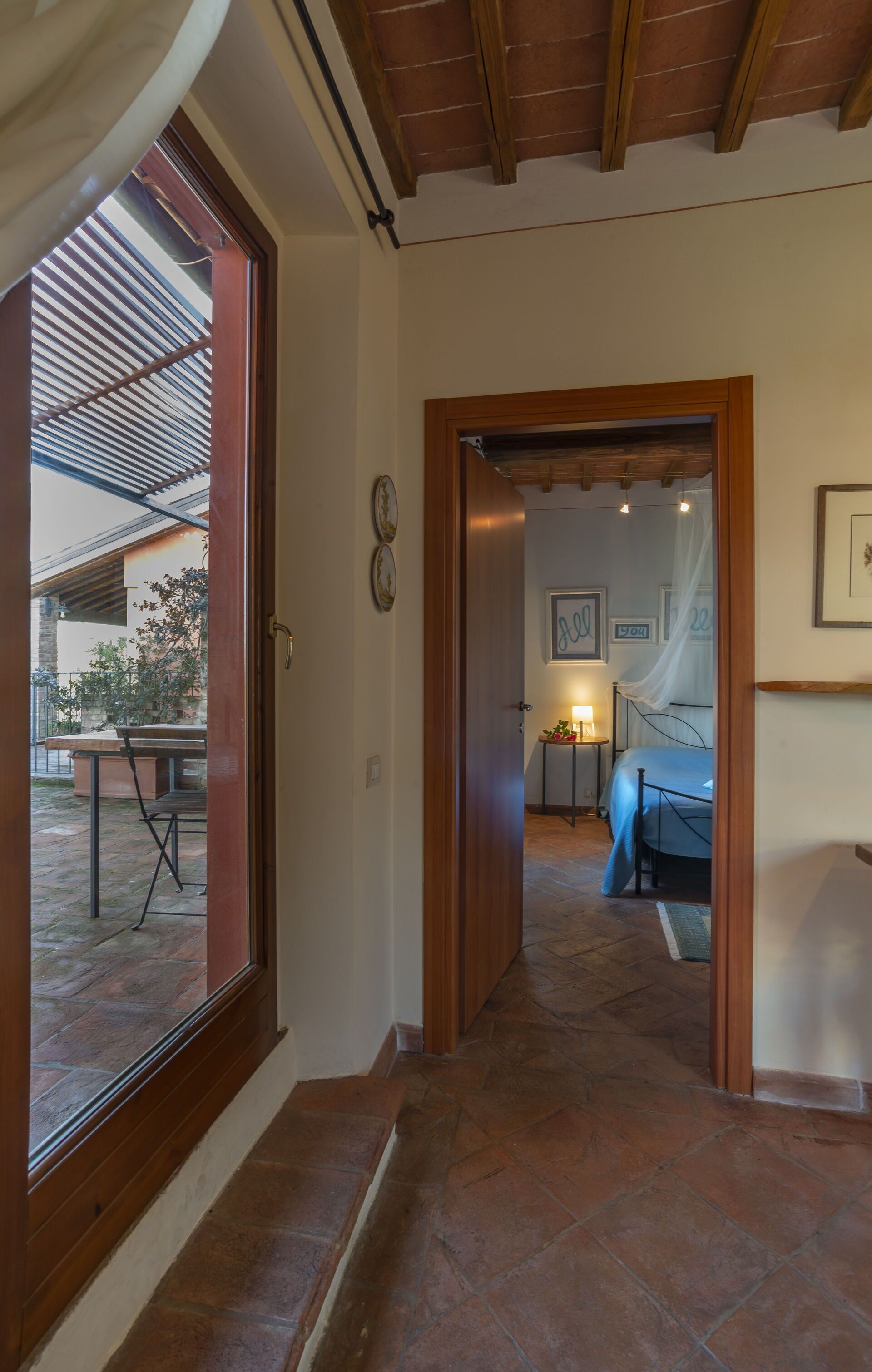 A hallway leading to a bedroom with a bed, a nightstand, and a picture on the wall.